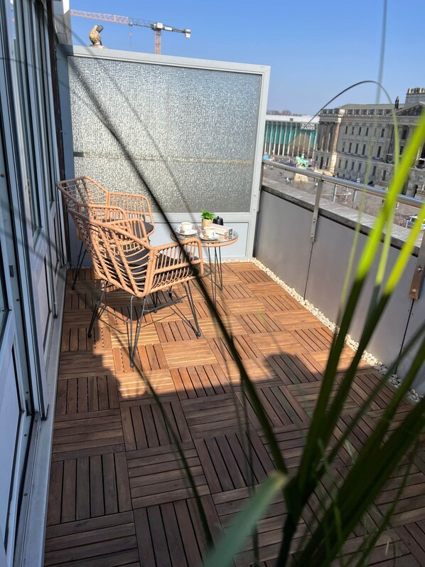 A balcony with a wooden floor, wicker furniture, and a view of the cityscape. - W&D Living-Tête de Fleur-Balcony above Schloßarkaden (Brunswick)