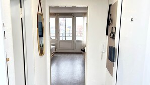 A hallway with a tiled floor, white walls, a door with a mirror, and a view into a room with a window and a radiator. - W&D Living-Tête de Fleur-Balcony above Schloßarkaden (Brunswick)