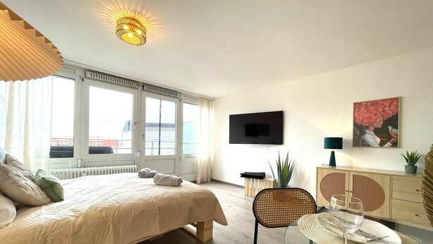 A modern bedroom with a large bed, a TV, and a dining area with a table and chairs. - W&D Living-Tête de Fleur-Balcony above Schloßarkaden (Brunswick)