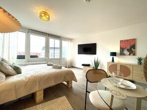 A modern bedroom with a large bed, a TV, and a dining area with a table and chairs. - W&D Living-Tête de Fleur-Balcony above Schloßarkaden (Brunswick)