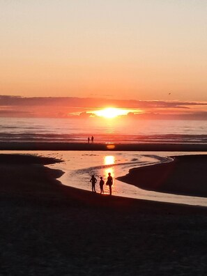 A beach scene with a sunset, people walking, and a calm sea. - Just Steps to the Sand - Sun of a Beach House (Rockaway Beach)