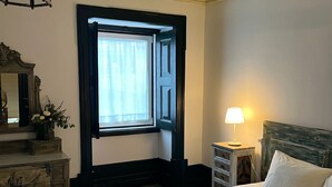 Ein ordentlich bezogenes Bett mit gefalteten Handtüchern, einer Nachttischlampe und einem Fenster mit Vorhängen.