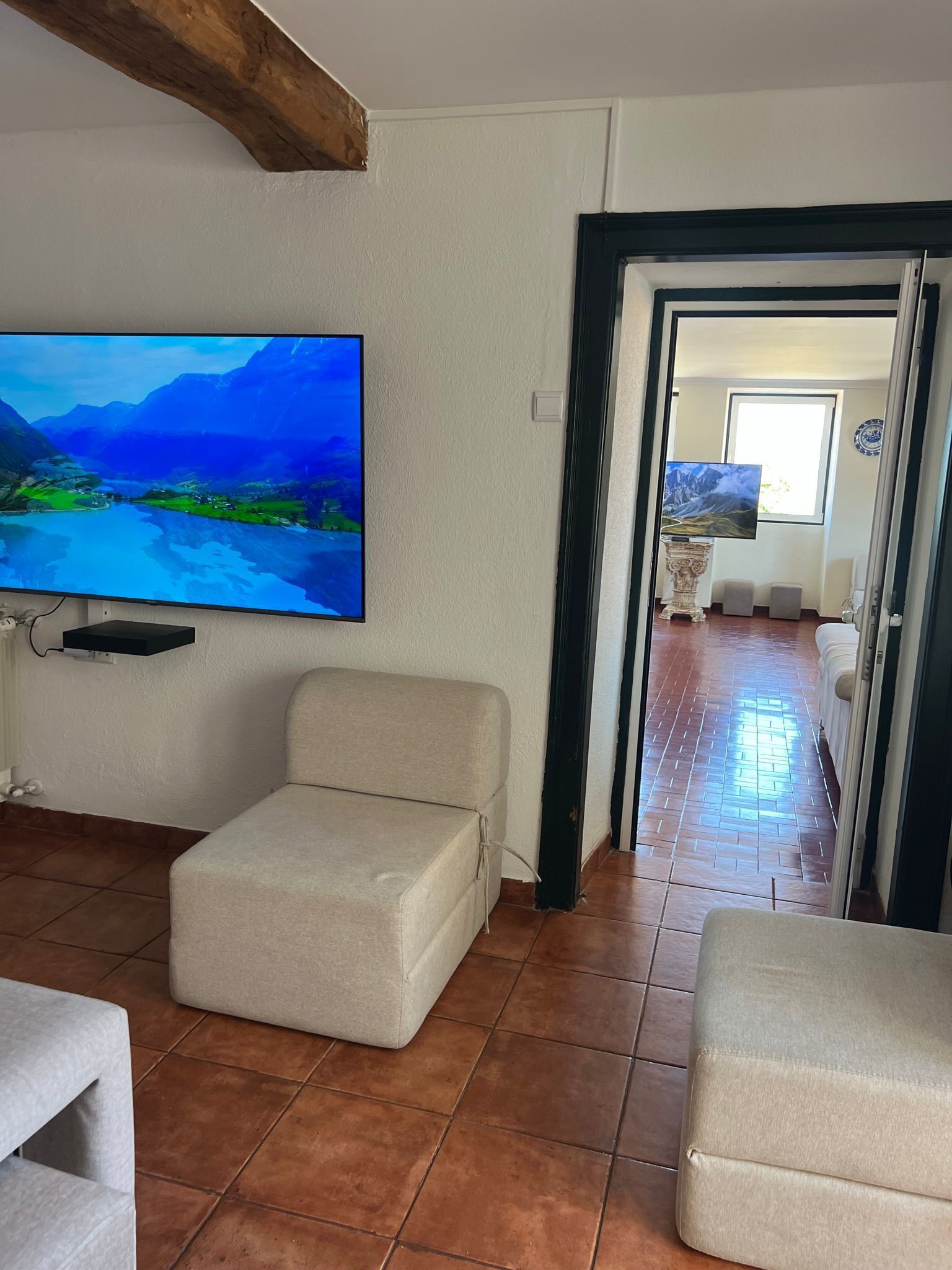 A living room with a flat-screen TV mounted on the wall, a beige sofa, and a tiled floor.