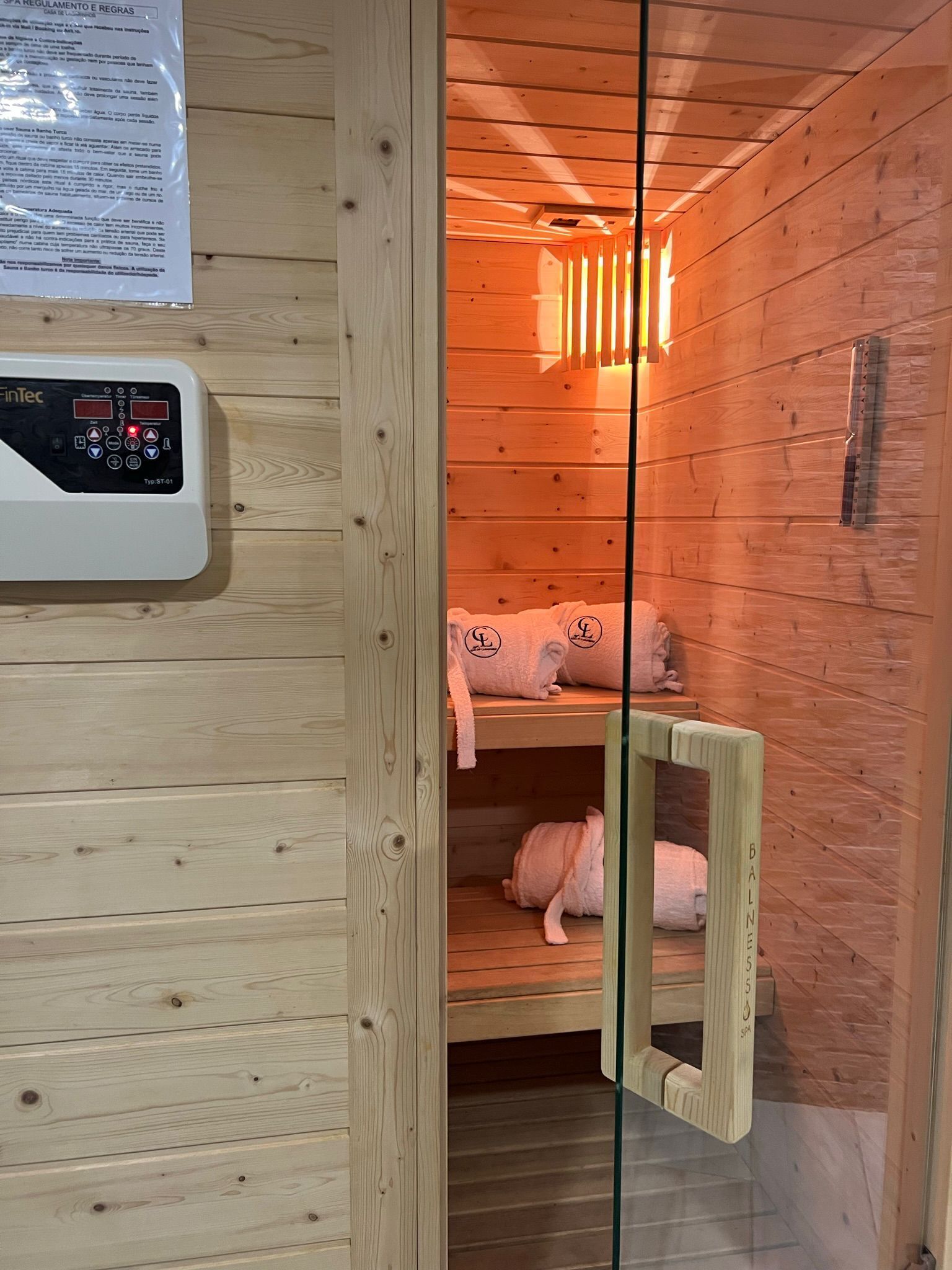 Eine Sauna mit Holzwänden, Bedienfeld und Handtüchern auf Ablagen.