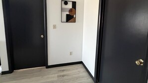Un pasillo con dos puertas negras, un interruptor de luz y una rejilla de ventilación en el techo.