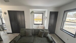 Una sala moderna con un sofá modular, una alfombra pequeña y vistas a un barrio residencial por la ventana.