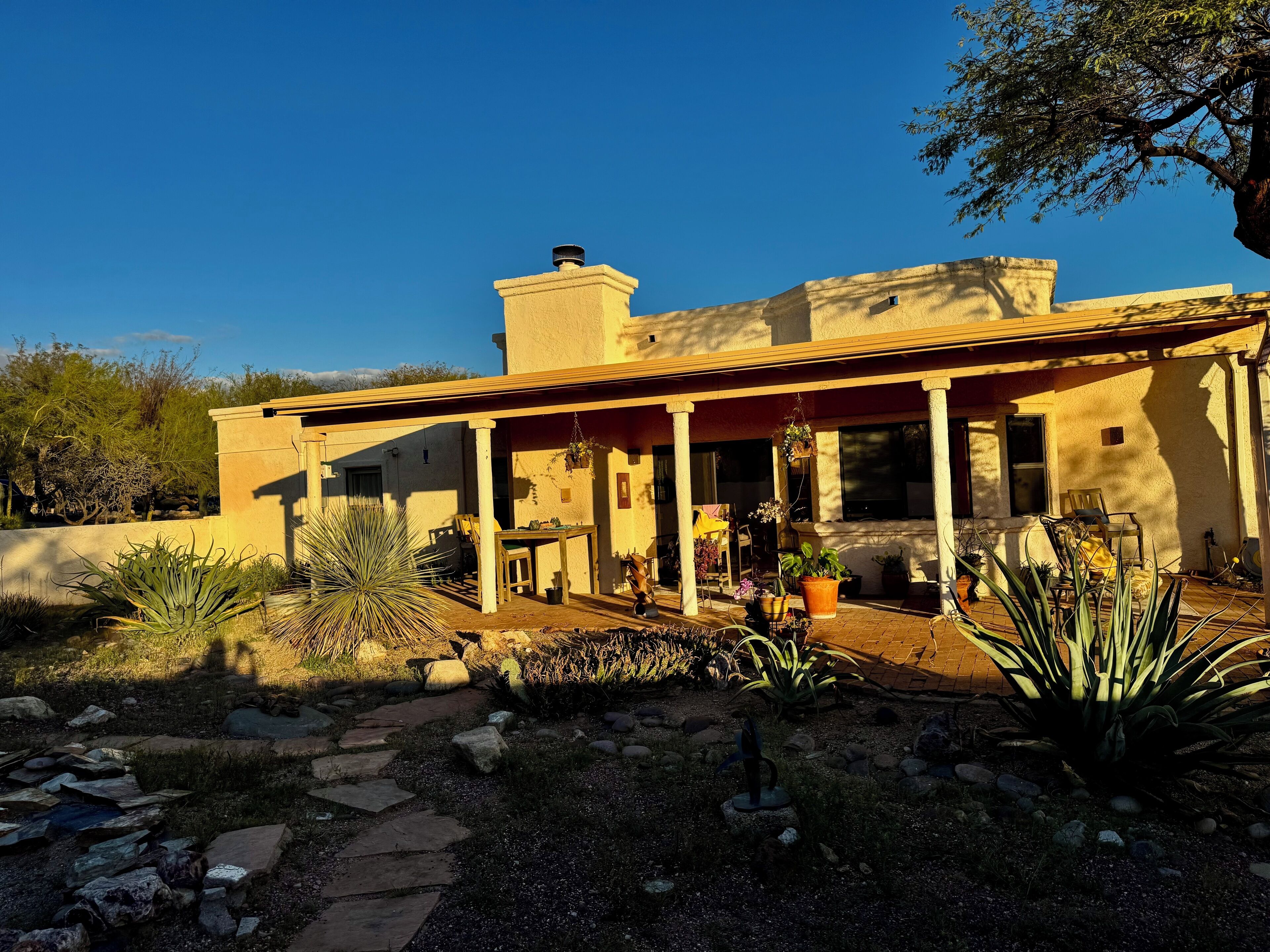 A two-story house with a covered patio, outdoor seating, and a variety of potted plants.