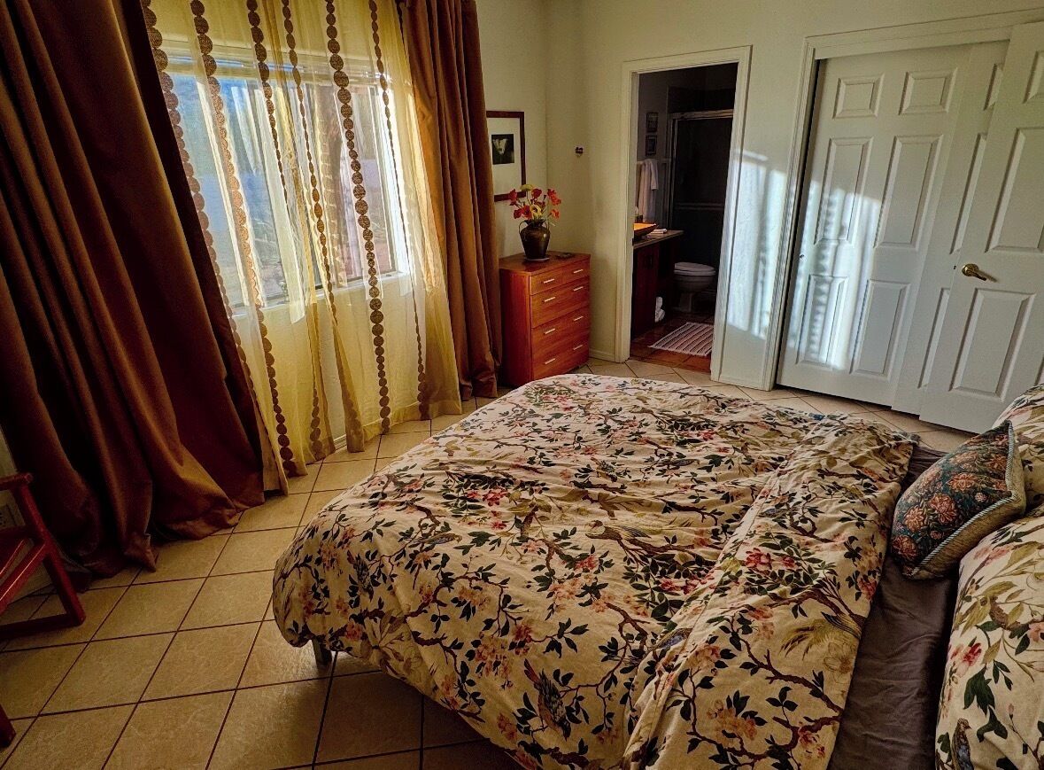 Een slaapkamer met een bloemenbedekking, een kaptafel, een vaas met bloemen en een deur naar een badkamer.