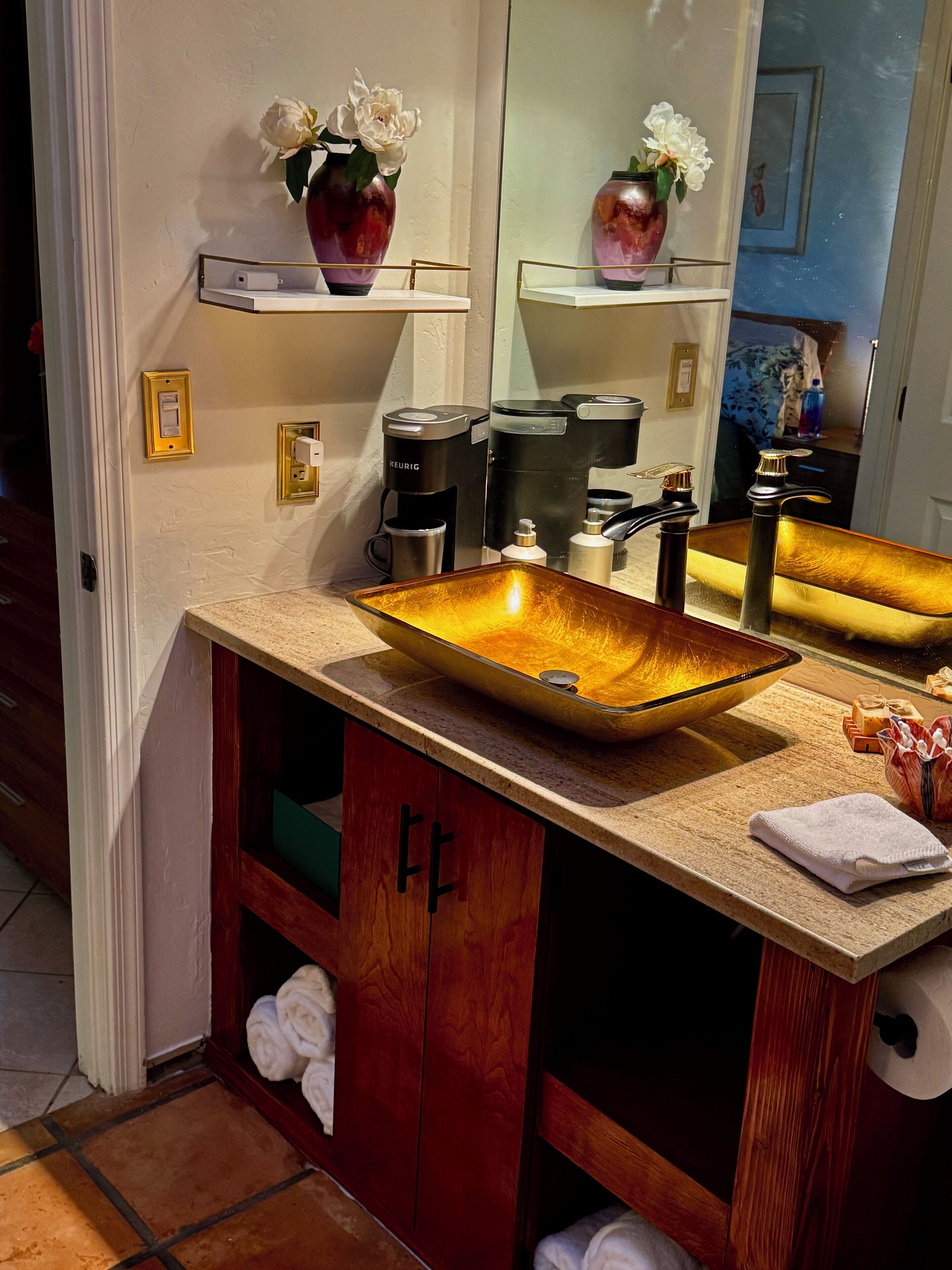 A bathroom with a large mirror, a vessel sink, and a coffee maker.