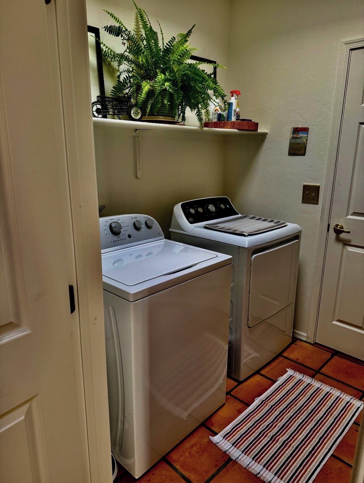 A laundry room with two washing machines, a drying rack, a plant, and a tiled floor.