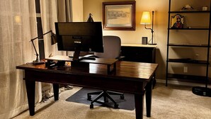 Une pièce comprenant un bureau, une chaise, un ordinateur, une lampe et un tableau encadré accroché au mur.