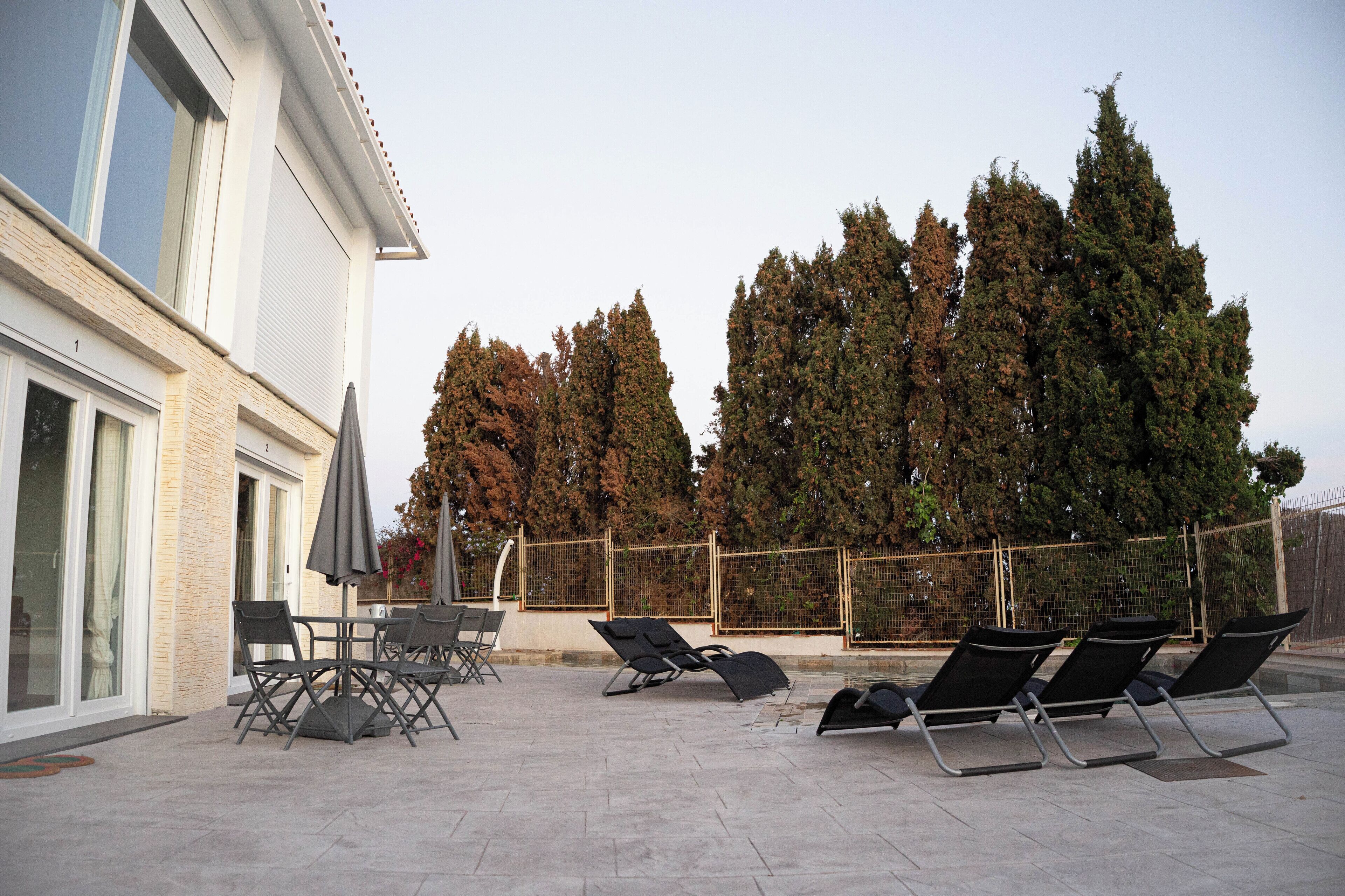 An outdoor patio with lounge chairs and a table, a fenced area, and tall trees.