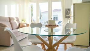 A dining area with a glass table surrounded by white chairs, a beige sofa, and a refrigerator. - Costa del Sol Villas - Bedroom with Private Bathroom 1 (Benajarafe)
