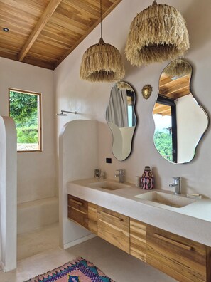 A modern bathroom with wooden beams, a large mirror, two hanging lights, and a view of greenery outside. - House with views of the jungle and the ocean (Santa teresa)