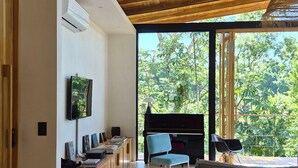 Una sala de estar moderna con un piano, un televisor y un amplio ventanal con vistas a un bosque.