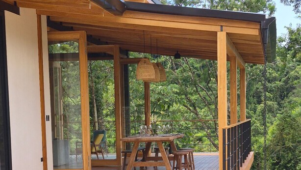 Un área de piscina moderna al aire libre con cubierta de madera, una mesa de comedor y sillas.
