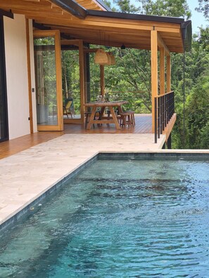 Un espace piscine extérieur moderne, doté d’une terrasse en bois, d’une table à manger et de chaises.