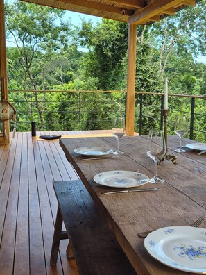 A wooden deck with a table set for dining, surrounded by lush greenery. - House with views of the jungle and the ocean (Santa teresa)