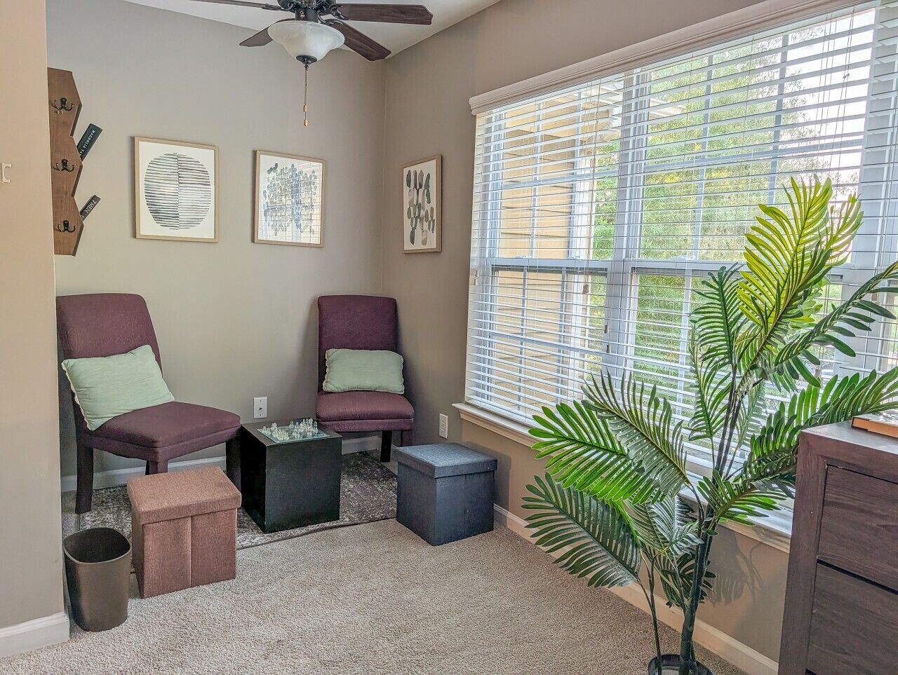A room with two chairs, a small table, a potted plant, and a window with blinds.