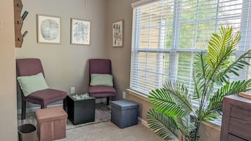 A room with two chairs, a small table, a potted plant, and a window with blinds.