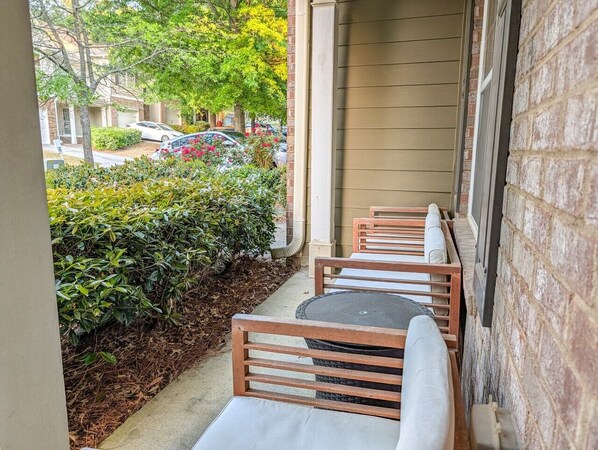 A covered outdoor seating area with wooden chairs and a table, leading to a building entrance.