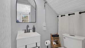 A bathroom with a white sink, mirror, and toilet. There is a window with a view of greenery outside.