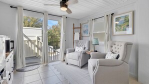 A spacious room with a balcony, a ceiling fan, and two armchairs with cushions.