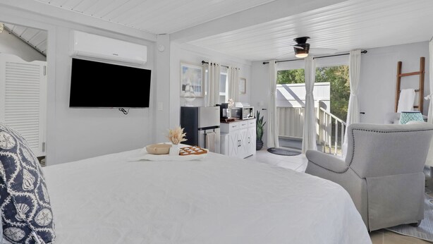 A bedroom with a large bed, a TV, a desk with a computer, and a balcony with a chair.