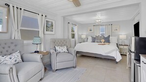 A bedroom with a large bed, two armchairs, a ceiling fan, and a TV.