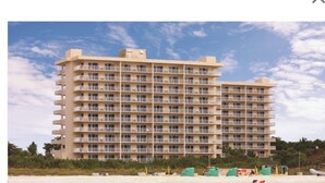 Un hotel de varios pisos con balcones, situado cerca de una playa con sombrillas y sillas.