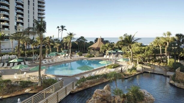 Zona de piscina en un resort con varias piscinas, palmeras y vistas al océano.