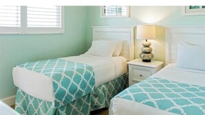 Una habitación con dos camas, cada una con una colcha estampada, una mesita de noche con lámpara y una ventana con persianas.