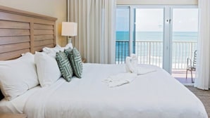 Un cuarto de hotel con una cama grande, un cabecero de madera, un balcón con vista al mar y una silla.