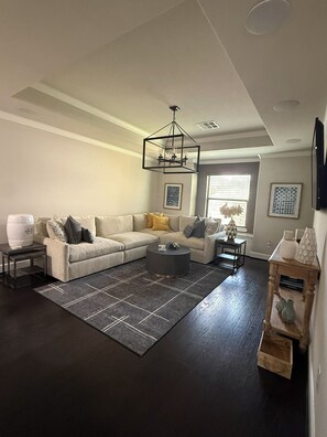 A living room with a sectional sofa, a coffee table, a rug, and a modern chandelier. - Montrose Area Home with Amenities and Comfort (Houston)