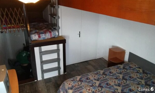Una habitación pequeña y funcional con una cama, una mesita y un armario.