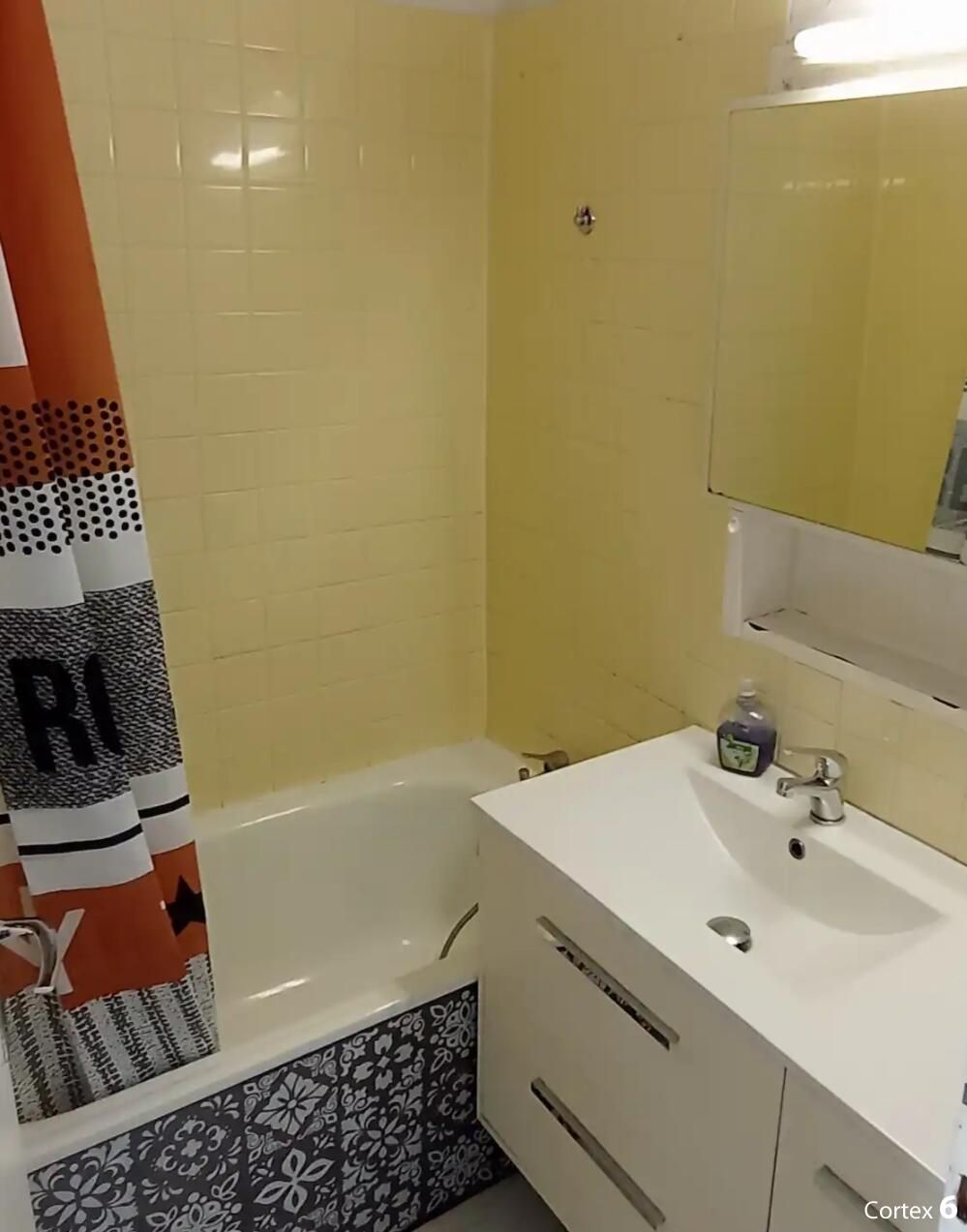 Ein Badezimmer mit einer Badewanne, einem weißen Waschbecken mit Spiegel und einem Boden mit gemusterten Fliesen.