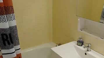 Ein Badezimmer mit einer Badewanne, einem weißen Waschbecken mit Spiegel und einem Boden mit gemusterten Fliesen.
