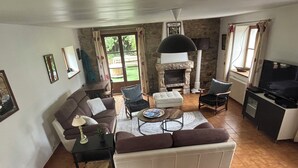Een woonkamer met een bank, fauteuils, een salontafel, een open haard en een televisie.
