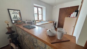 Een keuken met een stenen aanrecht, een witte waterkoker, twee witte mokken, een lijst met een foto en een raam met uitzicht op bomen.