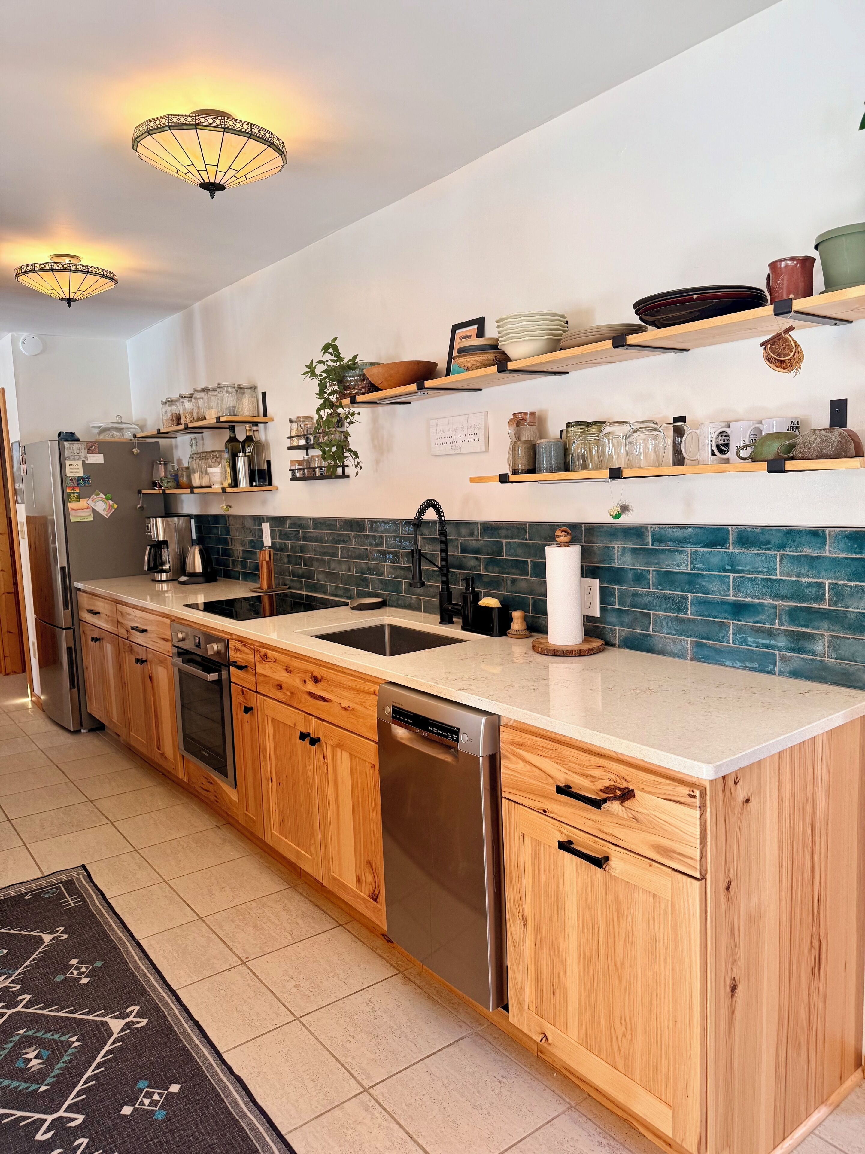 A modern kitchen with wooden cabinets, a stainless steel dishwasher, a double sink, and a backsplash with blue tiles.