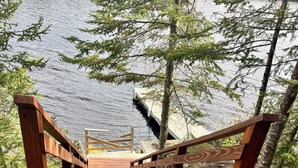 A wooden bridge leading to a dock over a body of water, surrounded by trees and rocks.