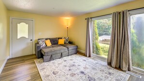Un salon comprenant un canapé d’angle, un tapis à motifs, une porte, une fenêtre avec des rideaux et une lampe fixée au mur.