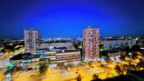 A high-rise building with multiple floors, surrounded by other buildings and a busy street with cars. - Peaceful 1-bedroom apartment in charming Novi Sad (Novi Sad)