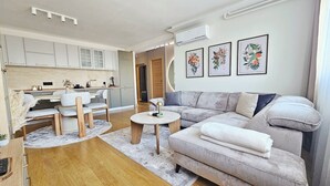 A modern living room with a grey sofa, wooden coffee table, and a kitchen area with white cabinets. - Peaceful 1-bedroom apartment in charming Novi Sad (Novi Sad)