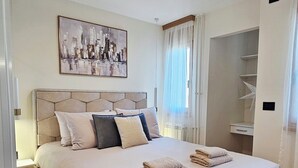 A neatly arranged bedroom with a large bed, a bedside table, a hanging artwork, and a window with sheer curtains. - Peaceful 1-bedroom apartment in charming Novi Sad (Novi Sad)