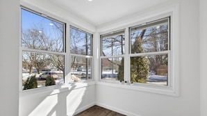 A corner room with three large windows, wooden flooring, and a view of a snowy landscape.