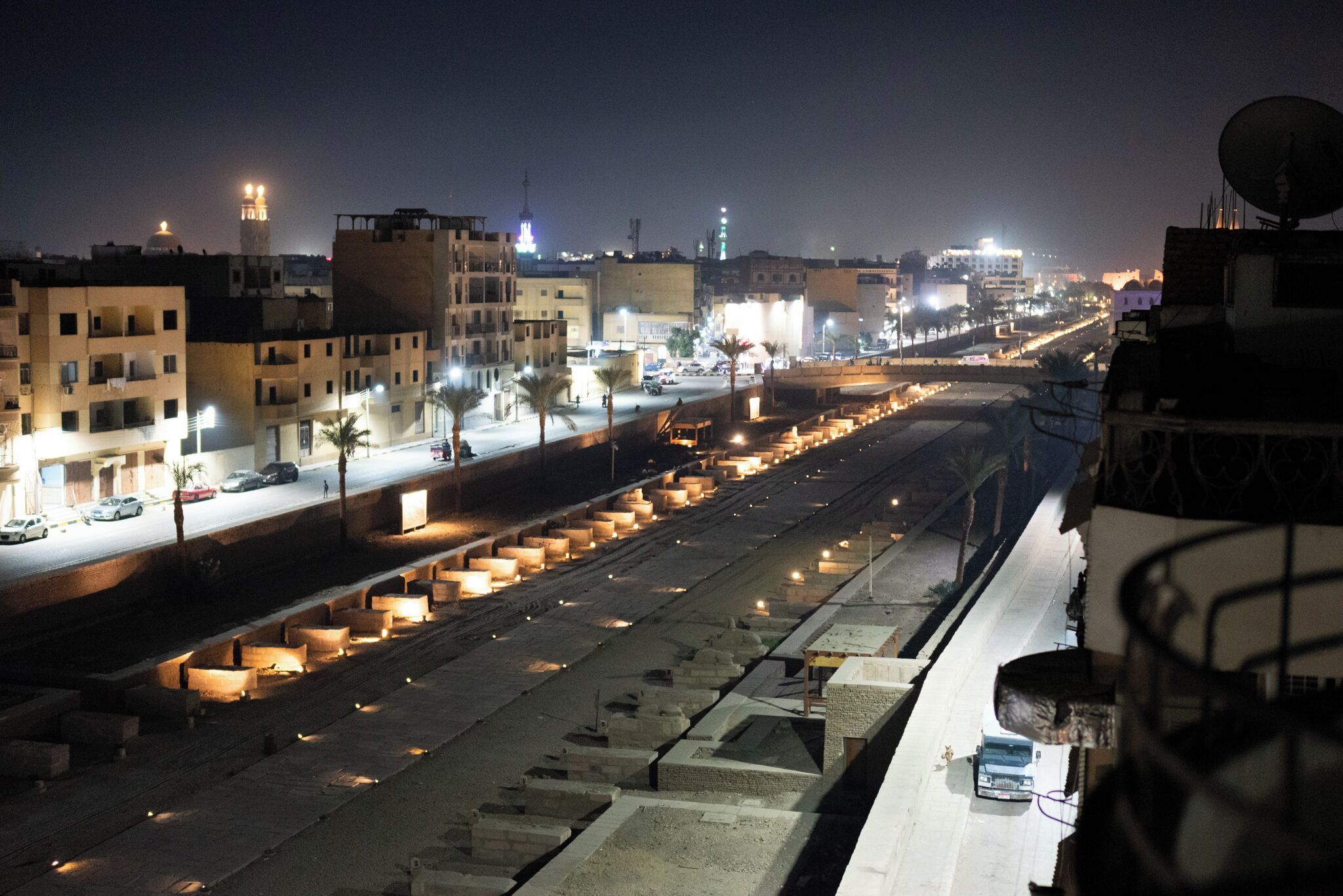 A nighttime cityscape with illuminated buildings, a busy road, and a clear view of the sky.