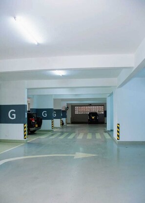 A parking garage with clear directional arrows on the floor, a few parked cars, and a gate with the letter 'G' on it. - Spacious 3br Apartment with Heated Swimming Pool (Nairobi)