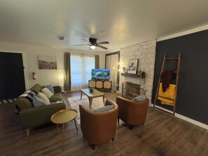 Ein Wohnzimmer mit einer Couch, Sesseln, einem Couchtisch, einem Fernseher, einem Kamin und einer Leiter.