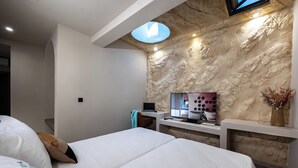 Quarto de hotel moderno com uma cama grande, uma mesa de trabalho com um laptop, uma televisão de tela plana e uma parede decorativa com textura.